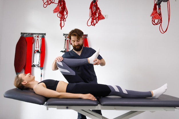 Doctor physiotherapist strectching the leg and knee of a female patient who lying on a massage table