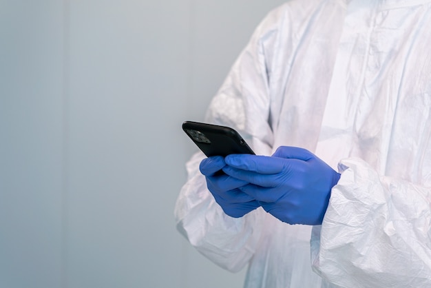 Doctor in PPE and using hand gloves consulting mobile application on smartphone during an pandemic of covid 19. Healthcare worker in personal protective equipments.