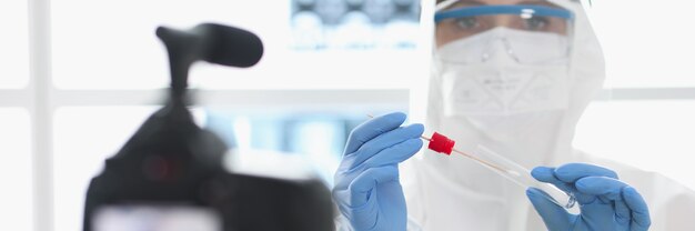 Doctor in protective suit demonstrates to camera test tube