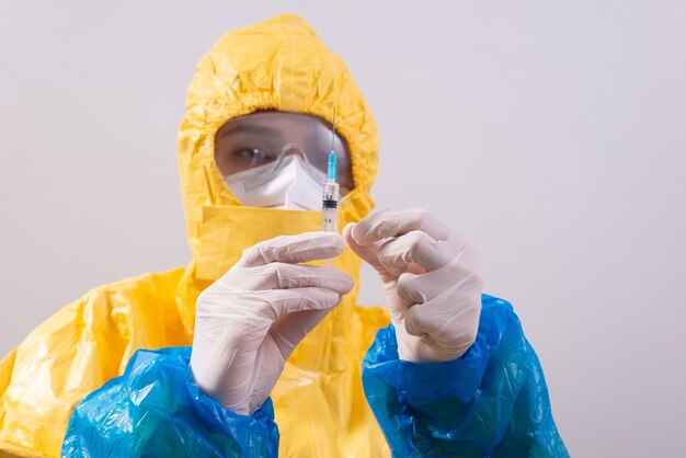 Doctor in a protective suit holds a vaccine on a white background