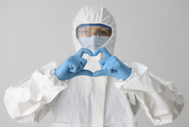 Doctor in protective suit and mask and glasses holds heart gesture danger zone and life concept