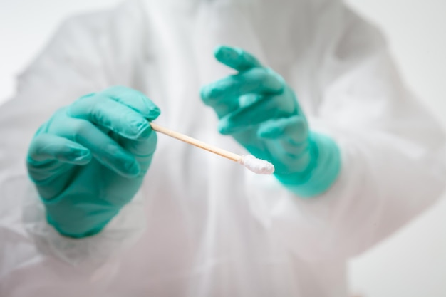 Doctor in protective suit PPE holding COVID-19 Nasal swab laboratory test. Medical worker performing Covid-19 test, taking nasal swab sample patient, PCR diagnostic, Rapid antigen test kit (ATK)