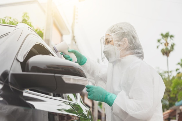 Doctor in protective suit PPE holding test kit. Medical worker performing drive-thru Covid-19 test, taking nasal swab sample patient through car window, PCR diagnostic, Rapid antigen test kit (ATK)