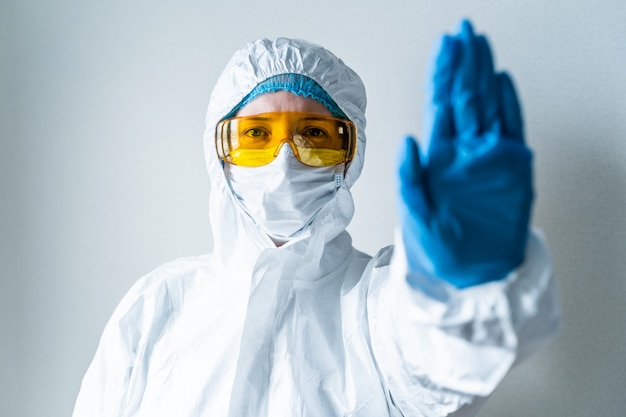 A doctor in a protective suit shows a stop sign. Pandemic concept of a new coronavirus