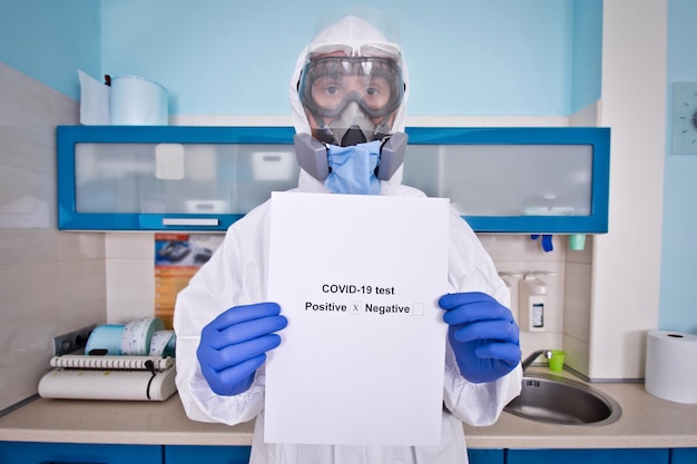 Doctor in protective suit uniform and mask holds coronovirus test results.