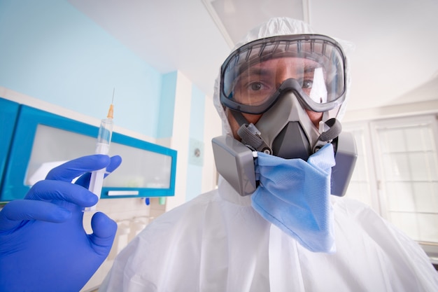 Doctor in protective suit uniform and mask holds injection syringe with vaccine.