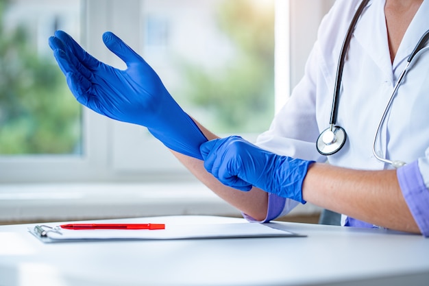 Doctor puts on blue rubber medical gloves for medical examination of a patient in a clinic. Health care and medicare