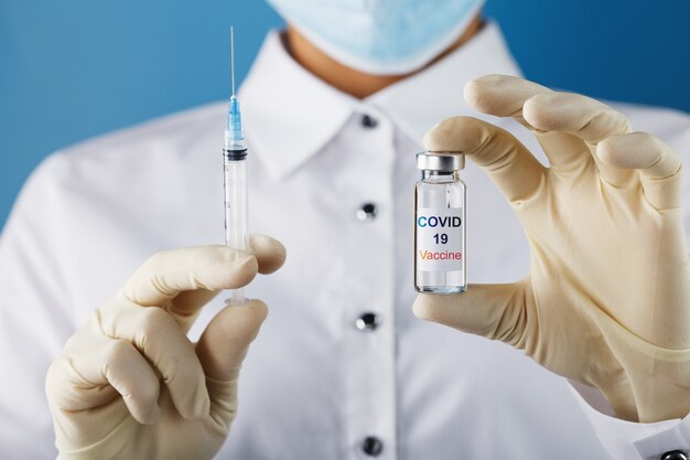 A doctor in rubber gloves takes medicine with a vaccine from an ampoule with a the text COVID -19