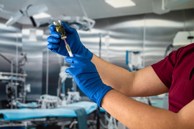 Doctor's hand in blue gloves hold medicine vaccine or anesthesia vial bottle and syringe preparing for surgery in the surgical office at the hospital