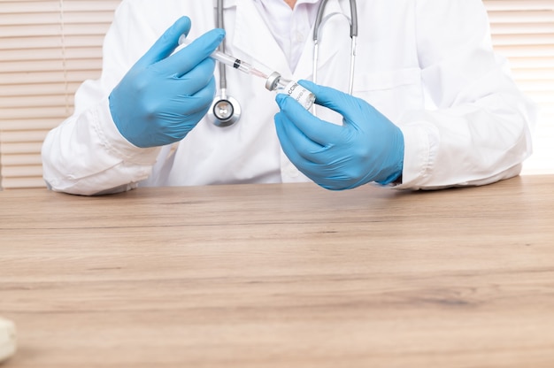 Doctor's hand holding vaccine vial and syringe of covid-19 on the doctor's desk