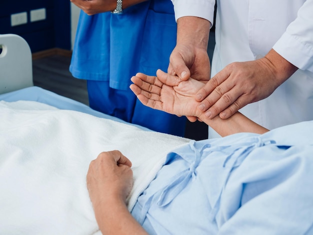 Doctor's hand in white lab coat is holding elderly patient's hand lying on the bed for check to examine heartbeat pulse by fingers in recovering room in hospital Medical health care checking concept