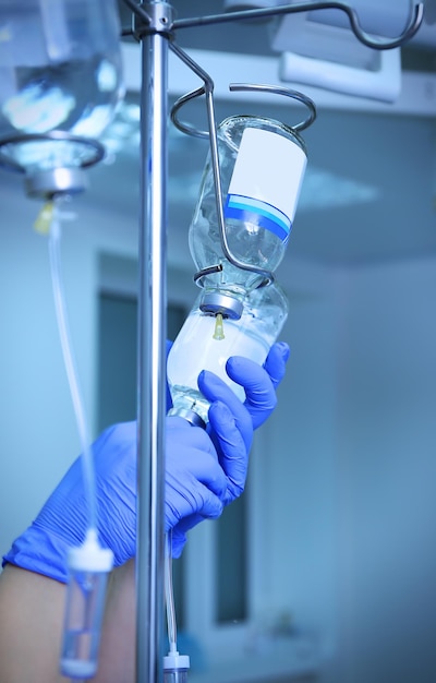 Doctor's hands and infusion drip in hospital on blurred background