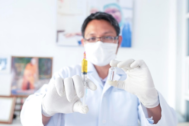 A doctor or scientist in a laboratory holding a syringe containing a liquid vaccine for a child or elderly person Concept disease medical treatment science