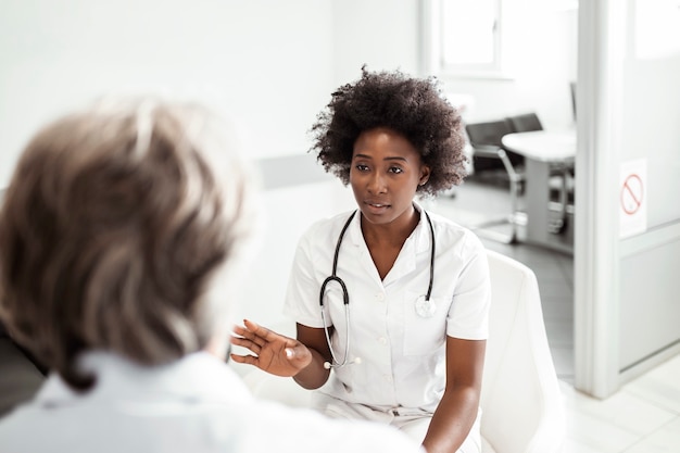 Doctor and senior man communicating while examining medical reports in a waiting room at medical clinic, hospital.