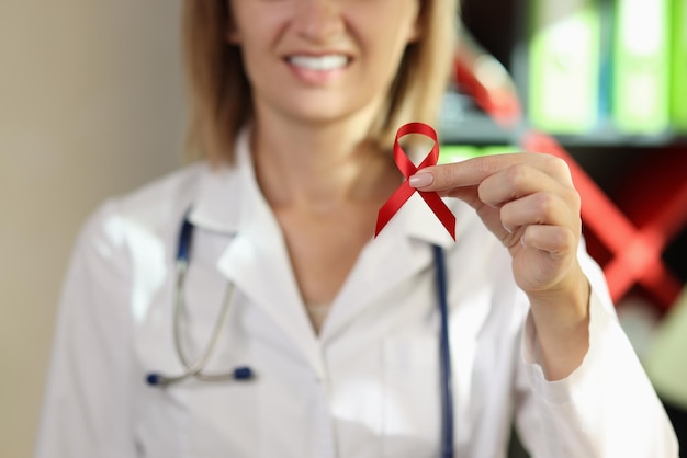 Doctor shows red ribbon as worlds aids day symbol in hospital office supporting patients with