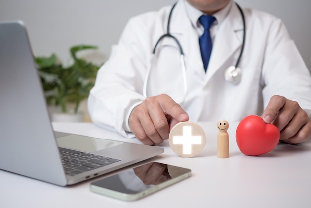 The doctor shows a wooden doll a plus sign and a red heart at the hospital Medical health care and medical services Insurance concept