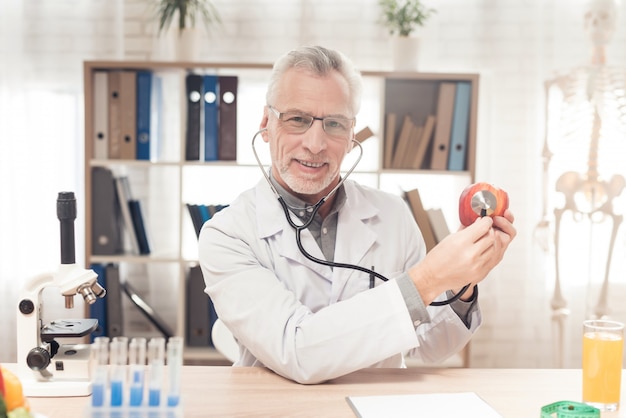 Doctor sitting at desk in office, listening apple.