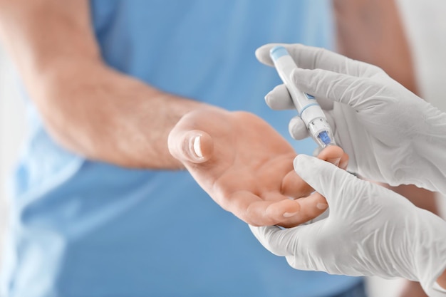 Doctor taking sample of diabetic patient's blood using lancet pen closeup