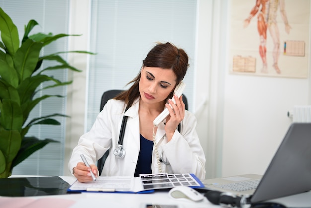 Doctor talking on the phone while writing on a document