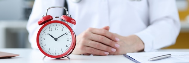 Doctor therapist sitting in office in front of red alarm clock closeup doctors schedule concept