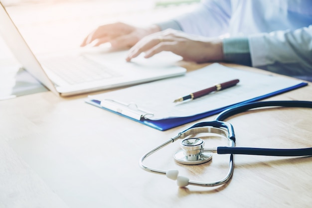 Doctor typing information on Laptop in Hospital office focus on Stethoscope