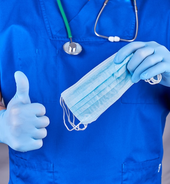 Doctor in uniform and in blue latex gloves keeps sterile masks, the other hand shows a gesture like