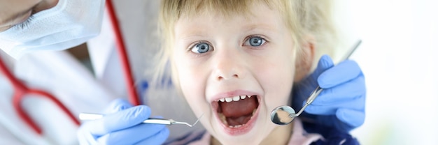 Doctor wearing protective mask examines jaw and mouth of little girl