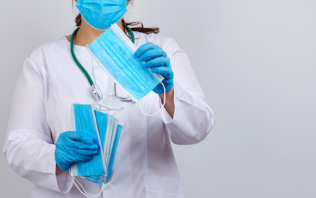 Doctor in a white coat and mask holds a stack of protective face masks about the virus