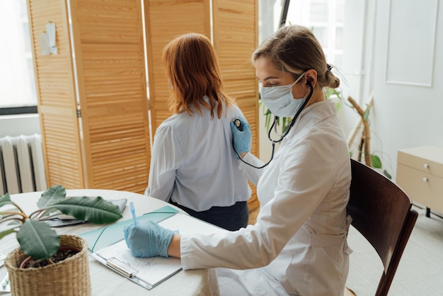 A doctor in a white coat and a mask is checking a patient's blood pressure.