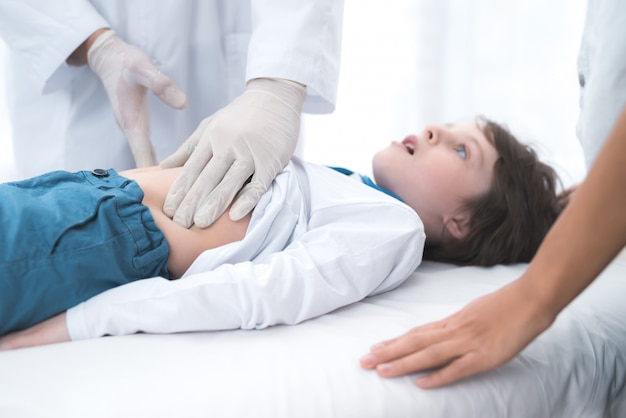 Doctor in white gloves massages the belly of a sick boy.