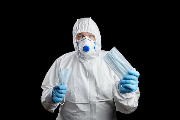 Doctor in white protective suit and facepiece respirator with medical face masks in hands