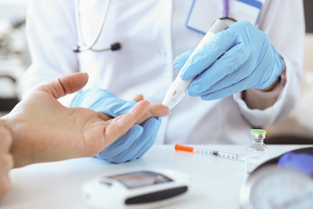 Doctor with gloves piercing patients finger with lancet closeup. Blood glucose monitoring