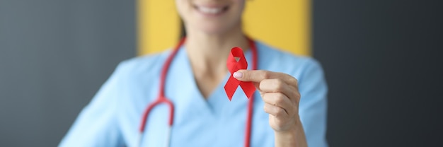 Doctor with stethoscope around neck holding red ribbon in clinic close-up