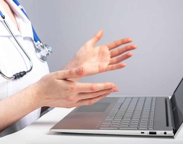 Doctor with stethoscope giving online consultation to patient Healthcare and telemedicine concept Woman in lab coat sitting at desk with laptop and advising people with illness remotely