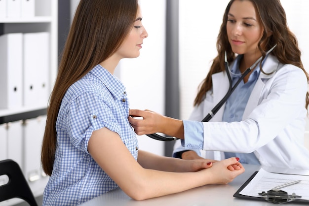 Doctor with a stethoscope in the hand examining her female patient. Health care, cardiology and medicine concepts.