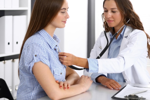 Doctor with a stethoscope in the hand examining her female patient. Health care, cardiology and medicine concepts.