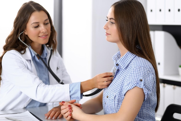 Doctor with a stethoscope in the hand examining her female patient. Health care, cardiology and medicine concepts.