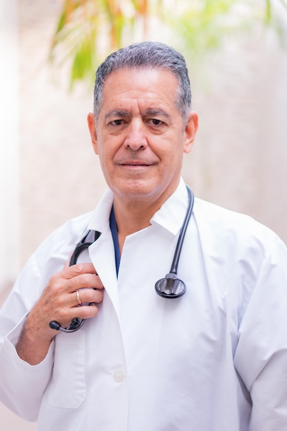 A doctor with a stethoscope on his neck stands in front of a plant.