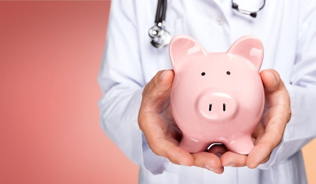 Doctor with stethoscope holding pink piggy bank