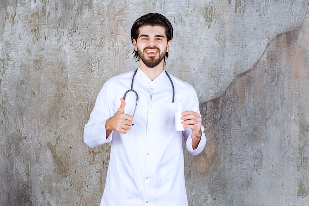 Doctor with a stethoscope holding a white tube of hand sanitizer spray and showing thumb up sign. 