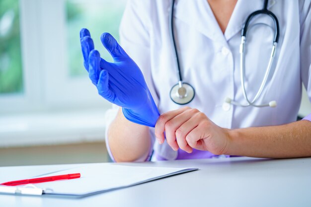 Doctor with stethoscope puts on blue rubber medical gloves for medical examination of a patient in a hospital