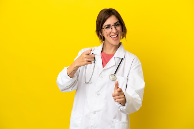 Doctor woman isolated on yellow background pointing to the front and smiling