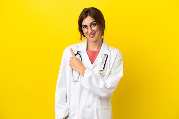 Doctor woman isolated on yellow background pointing to the side to present a product