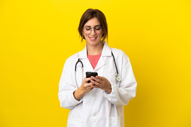 Doctor woman isolated on yellow background sending a message with the mobile