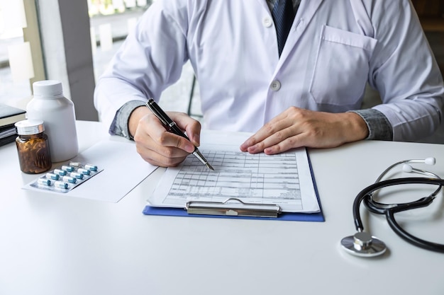 Doctor working and writing on paper report in hospital and medical stethoscope, medicine on clipboard on desk.