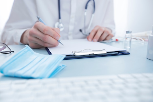 Doctor writes a prescription while sitting at the table. 