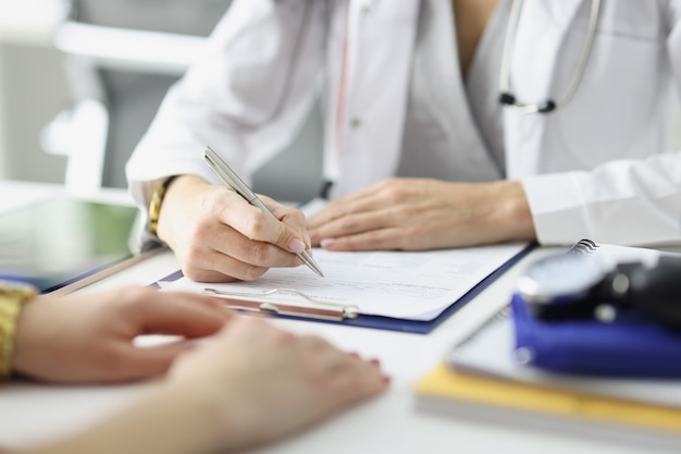 Doctor writing information into documents in front of patient at clinic closeup medical history