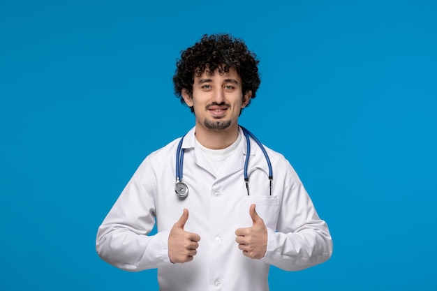 Doctors day curly handsome cute guy in medical uniform holding good gesture sign