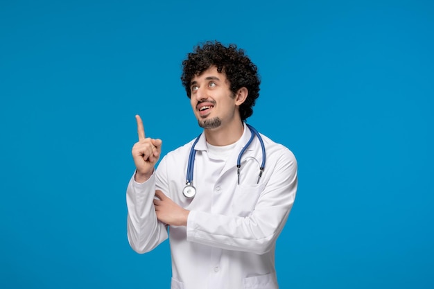 Doctors day curly handsome cute guy in medical uniform pointing up