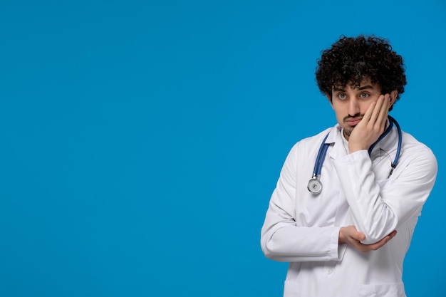 Doctors day curly handsome cute guy in medical uniform thinking confusingly